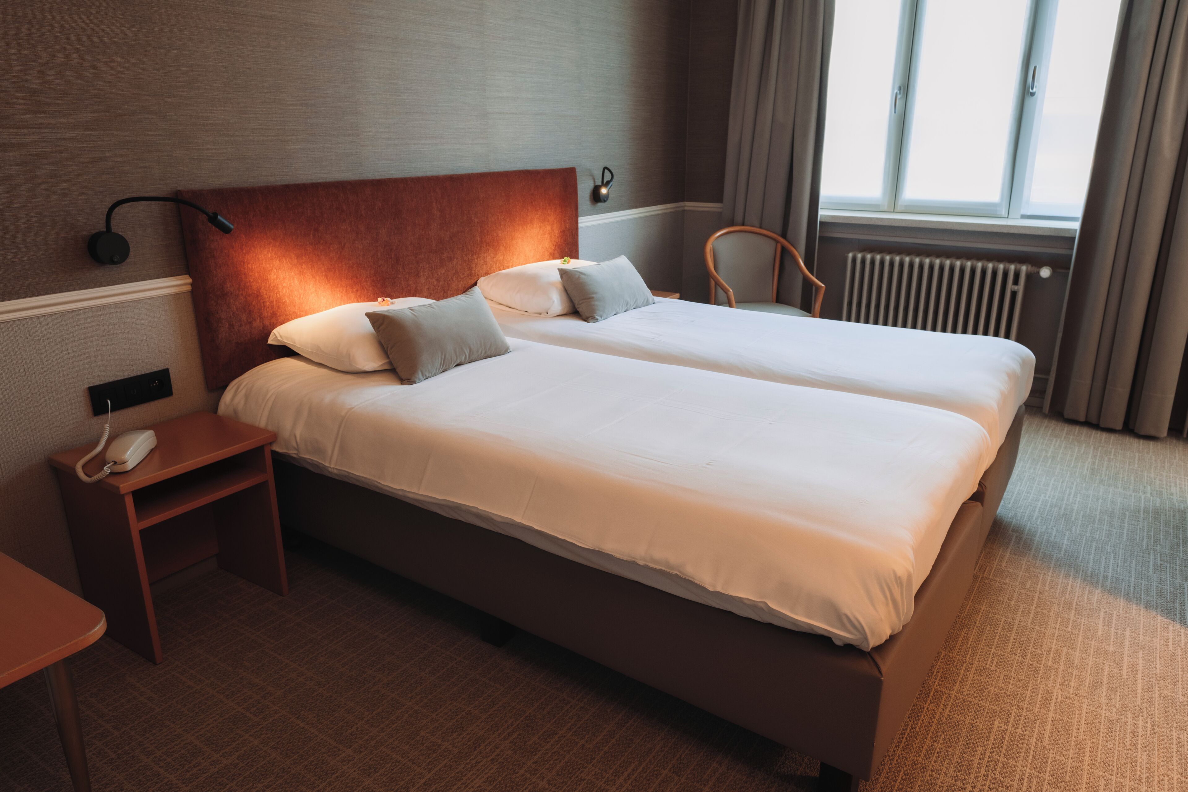 A double bed with a headboard, bedside tables, a telephone, and a window with curtains.