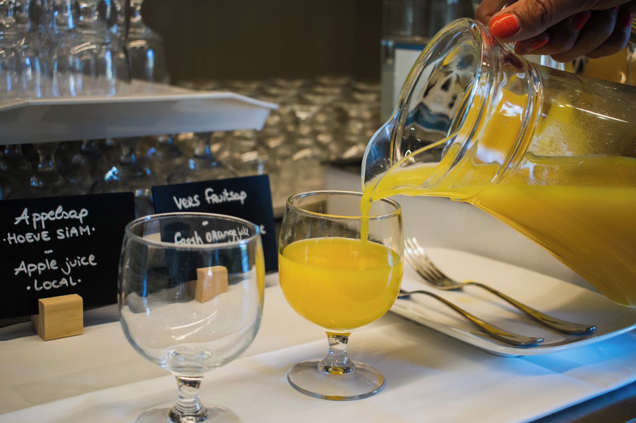Un bicchiere che viene riempito con un liquido giallo, probabilmente succo, in un contesto con un cartello che recita 'Succo di mela locale'.