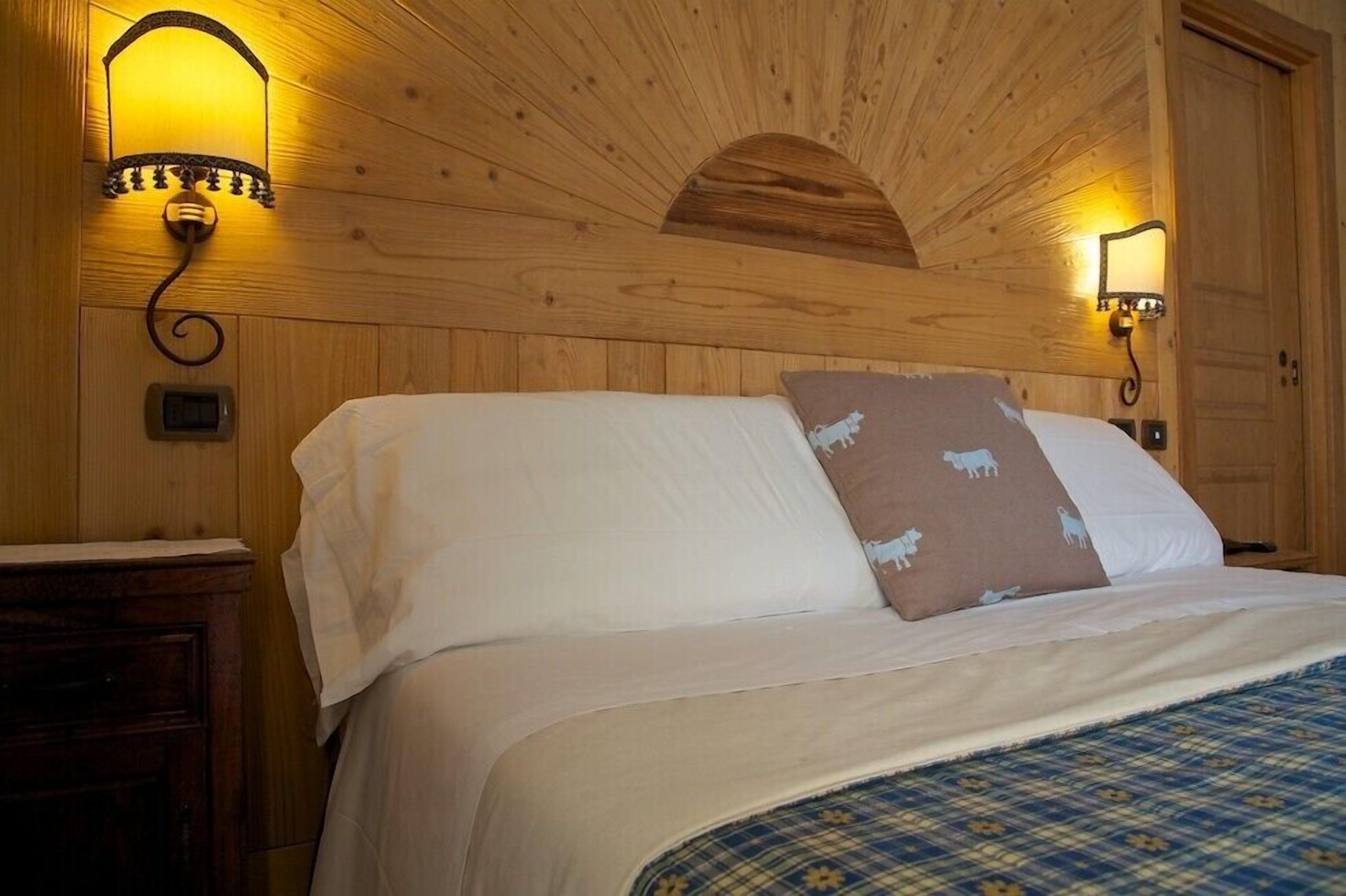 Una habitación con paneles de madera, una cama, dos lámparas fijadas a la pared y un pequeño mueble de madera.