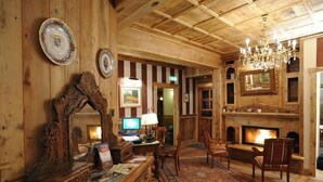 A wooden interior with a fireplace, a chandelier, and a desk with a computer. - Hotel Laghetto (Brusson)