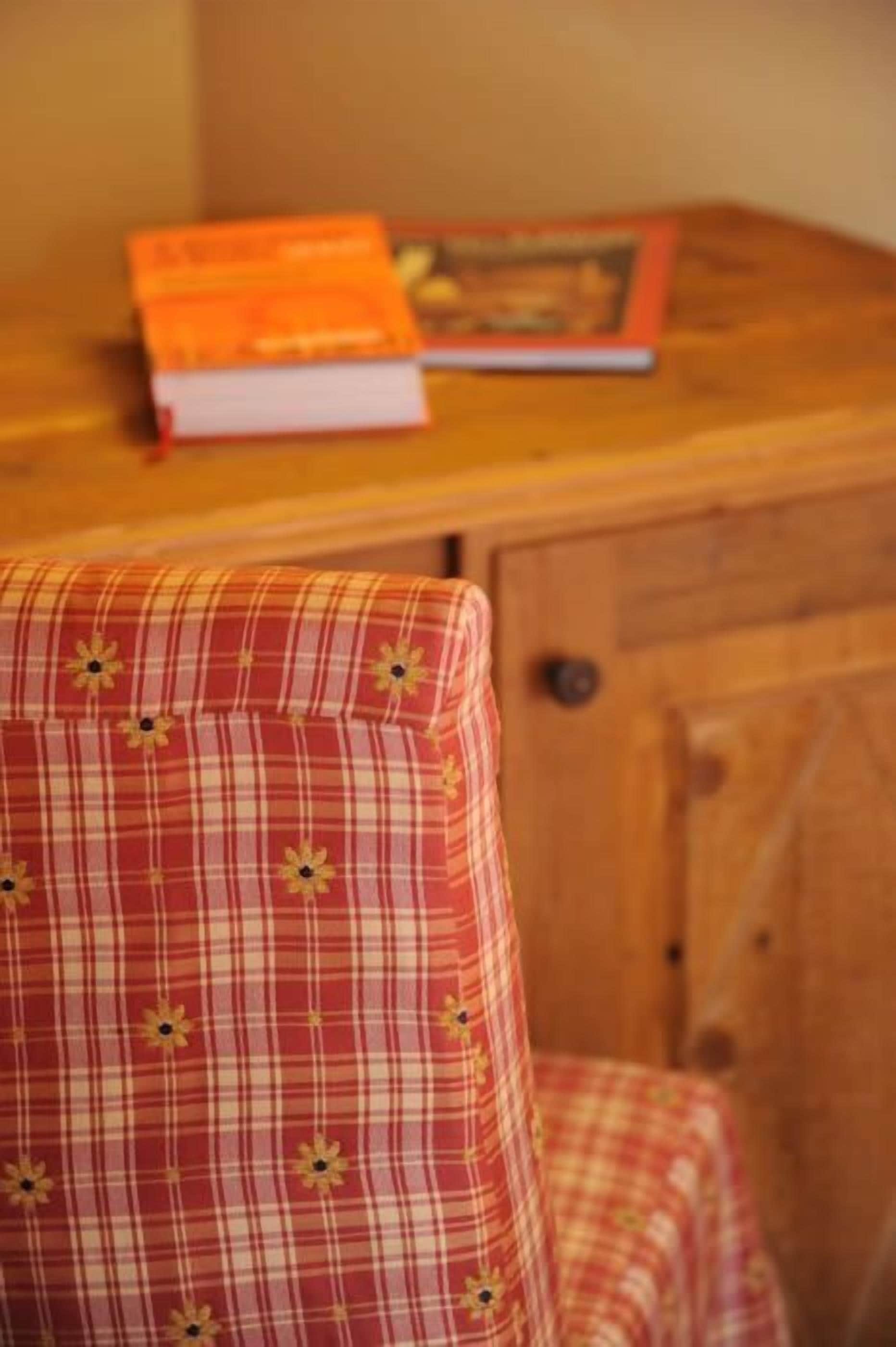 Una silla con estampado de cuadros y diseño floral, una mesa de madera con un libro encima y un armario de madera al fondo.
