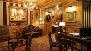 A cozy, wood-paneled room with a vintage sofa, chairs, a desk, and a chandelier. - Hotel Laghetto (Brusson)