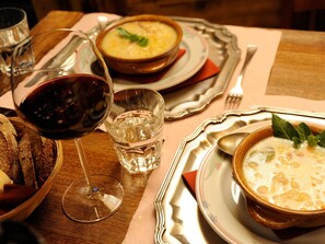 Una mesa de comedor con un tazón de sopa, una copa de vino y un cesto de pan.
