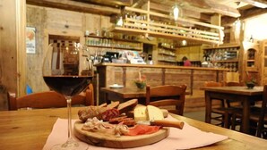 A wooden interior with a wooden table displaying a charcuterie board, a glass of red wine, and a rustic bar area in the background. - Hotel Laghetto (Brusson)