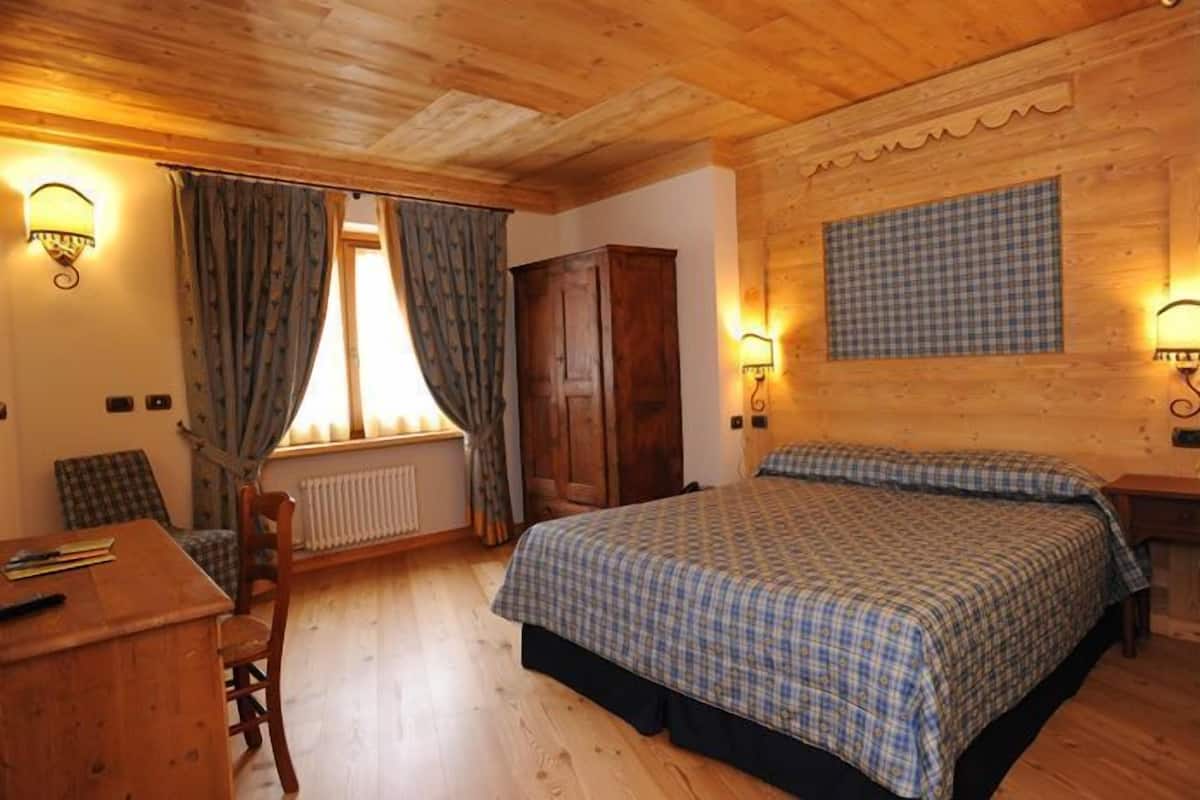 A wooden-paneled room with a bed, a desk, and a chair.