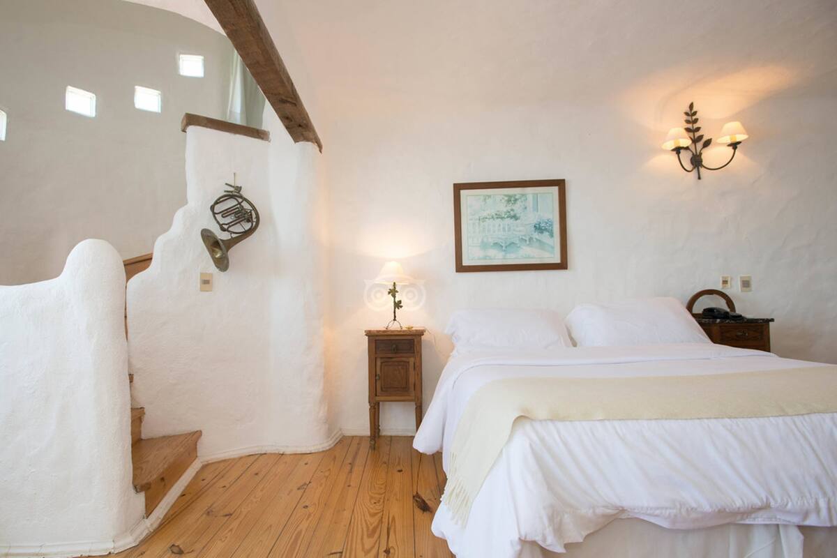Een slaapkamer met een houten trap, een bed, een nachtkastje, een wandlamp en een lijst met een afbeelding.