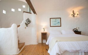 Quarto com escada de madeira, uma cama, mesa de cabeceira, luminária na parede e um quadro emoldurado.
