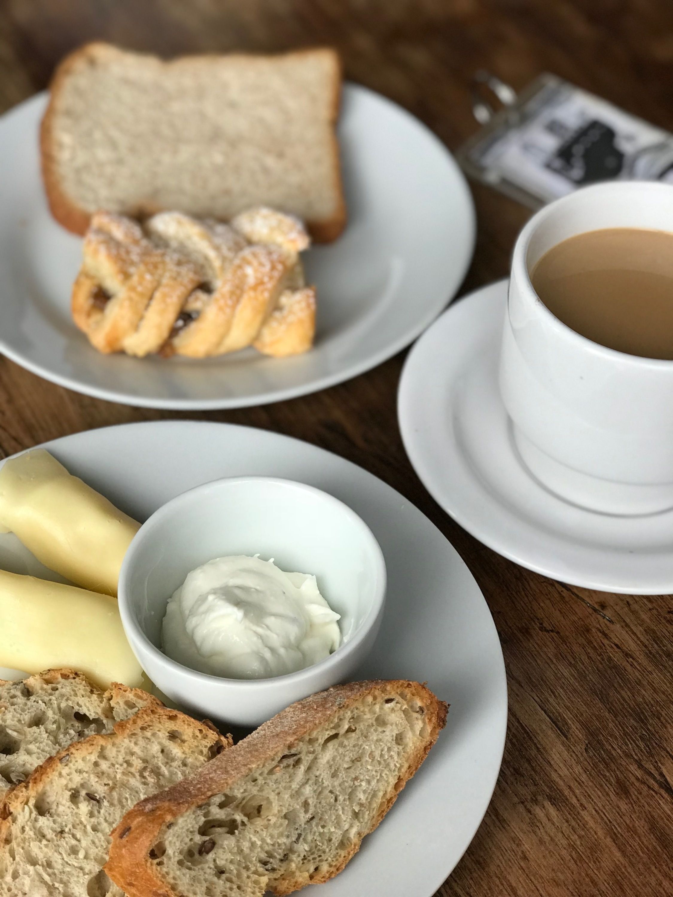 Ein Tisch mit Brot, ein Schälchen Frischkäse und eine Tasse Kaffee.
