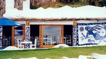 Un restaurante con terraza, sillas blancas y una sombrilla azul.