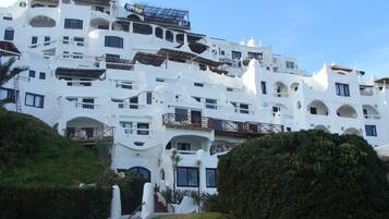 A white, multi-story hotel with balconies and a staircase leading to the entrance.