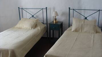 Two twin beds with a metal headboard design, a bedside table with a lamp, and a plain wall in the background.