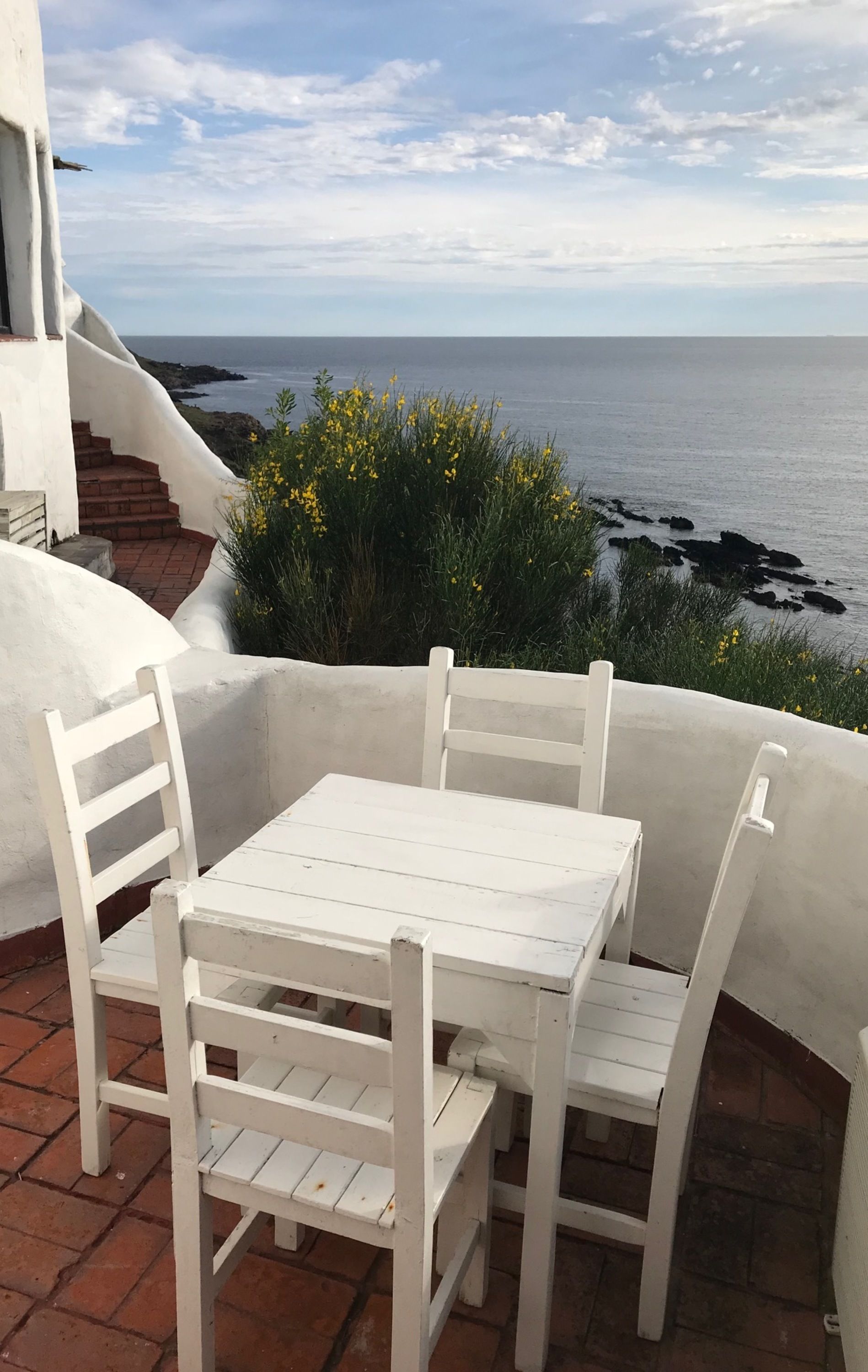 A white table and chairs on a terrace with a view of the sea.