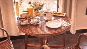 Un tavolo da pranzo con cibi per la colazione, sedie in vimini e vista sul mare.