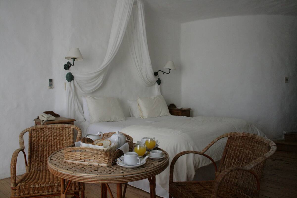 Een kamer met een bed, twee rieten stoelen, een kleine ronde tafel met ontbijtartikelen en een hemelbed.