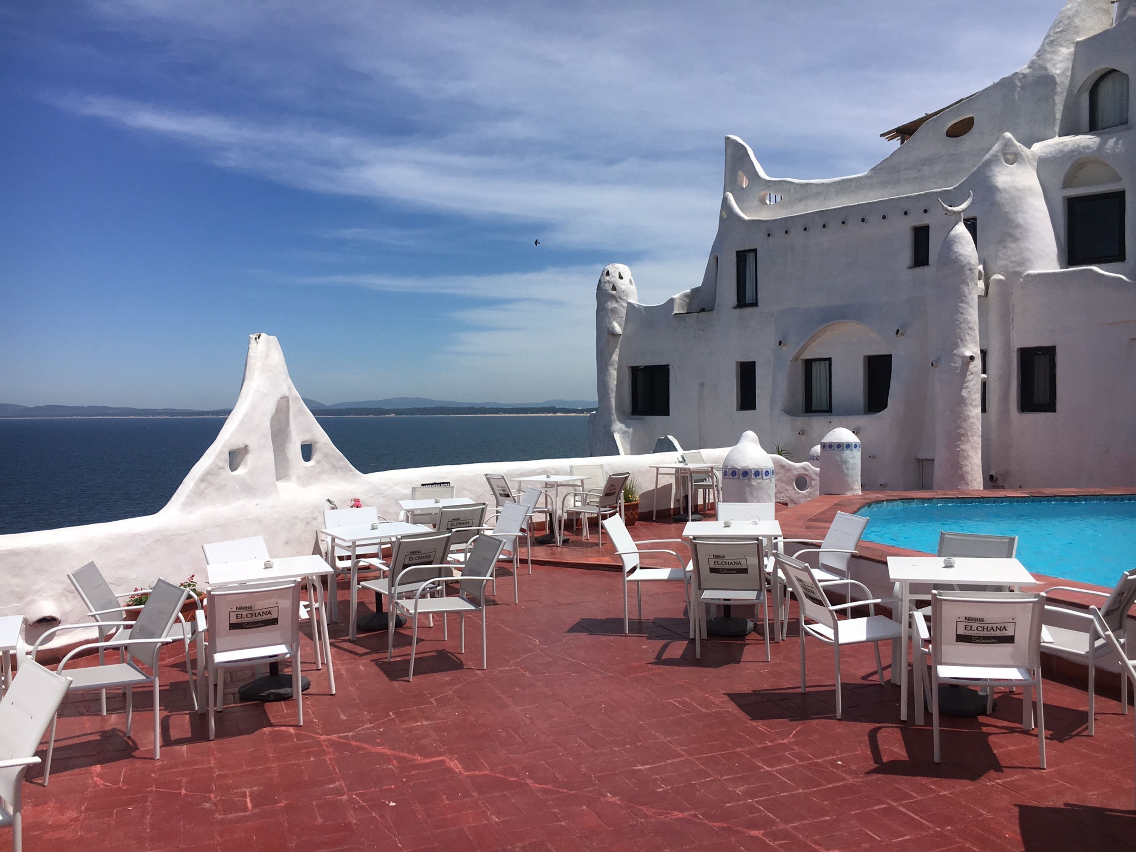 Une terrasse sur le toit, avec des chaises et des tables blanches, une piscine et une vue sur la mer.