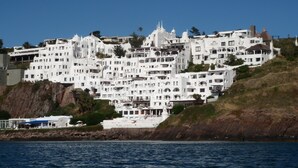 Un complesso di edifici costieri con diverse strutture bianche, alcune dotate di balconi, situato su una collina con vista sul mare.
