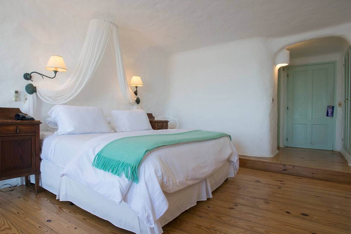 Een slaapkamer met een bed, nachtlampjes, een houten nachtkastje en een groene plaid.