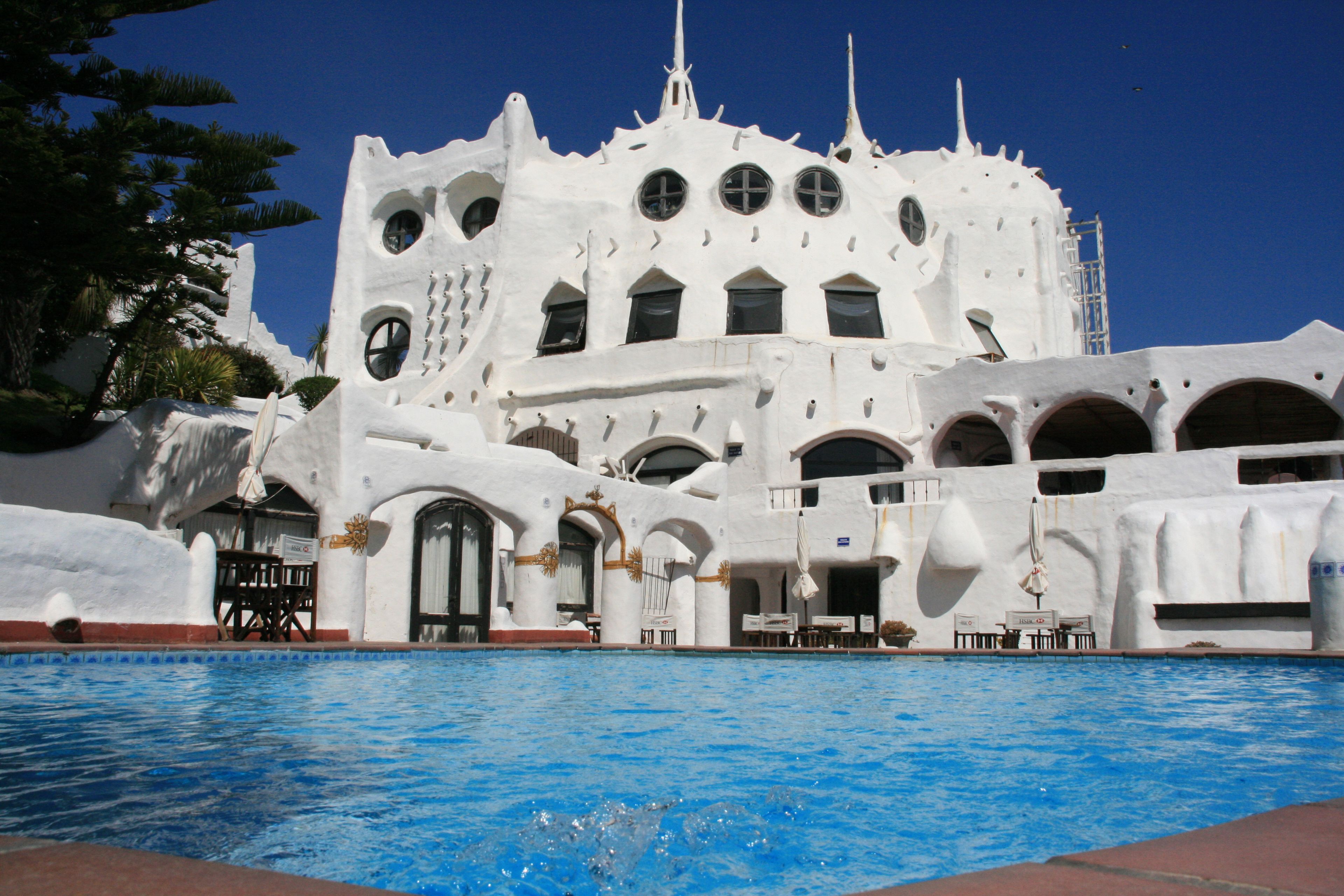 Un edificio blanco con varios ventanales arqueados y una piscina al frente.