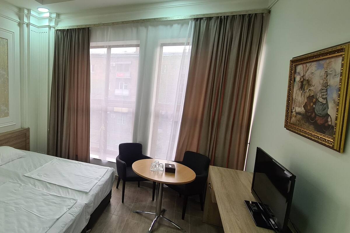 Une chambre d’hôtel avec un lit, un bureau et une chaise, une table avec des verres et un tableau au mur.