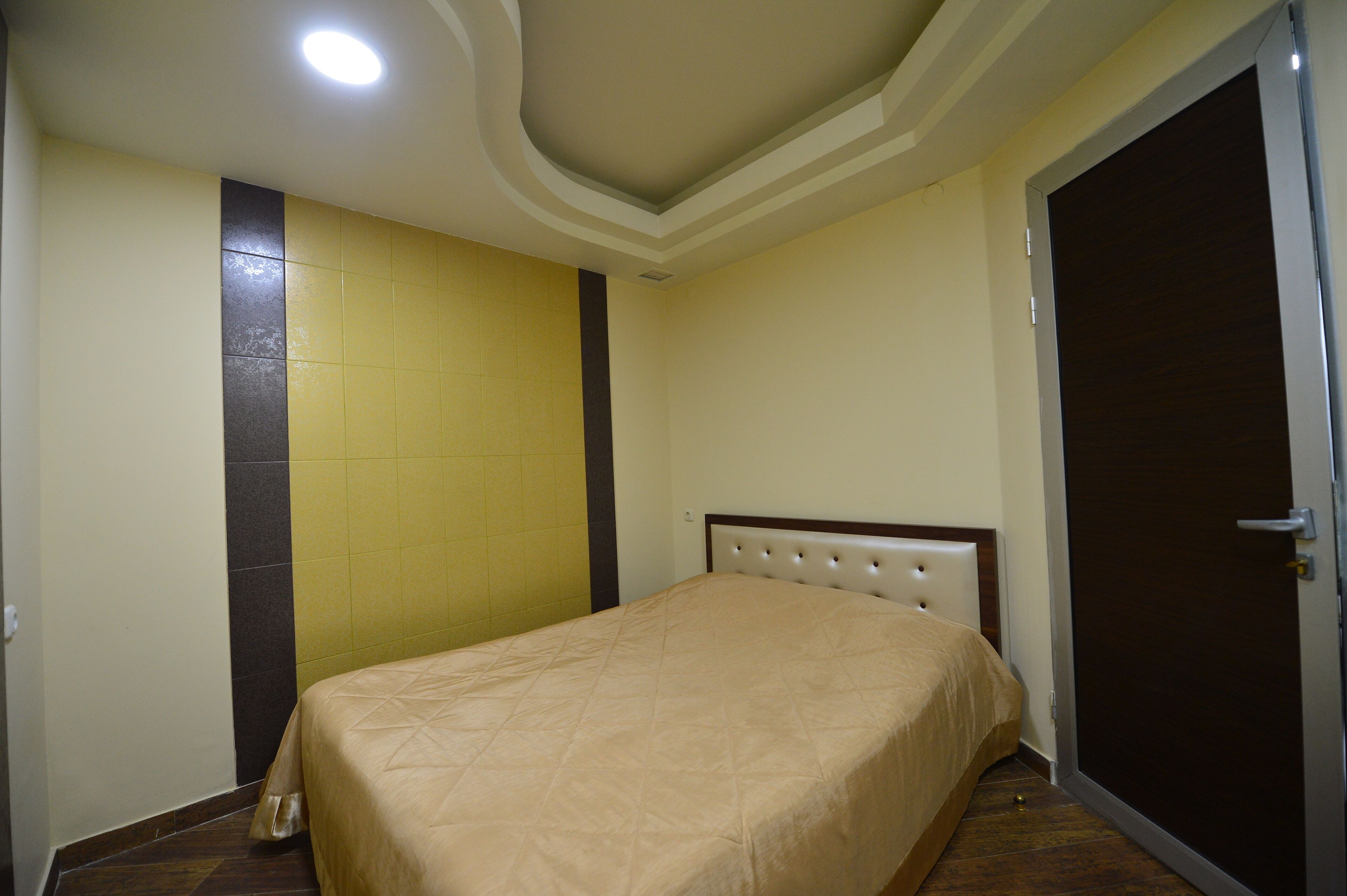 A bedroom with a bed, a door, and a wall with a vertical strip of dark tiles.