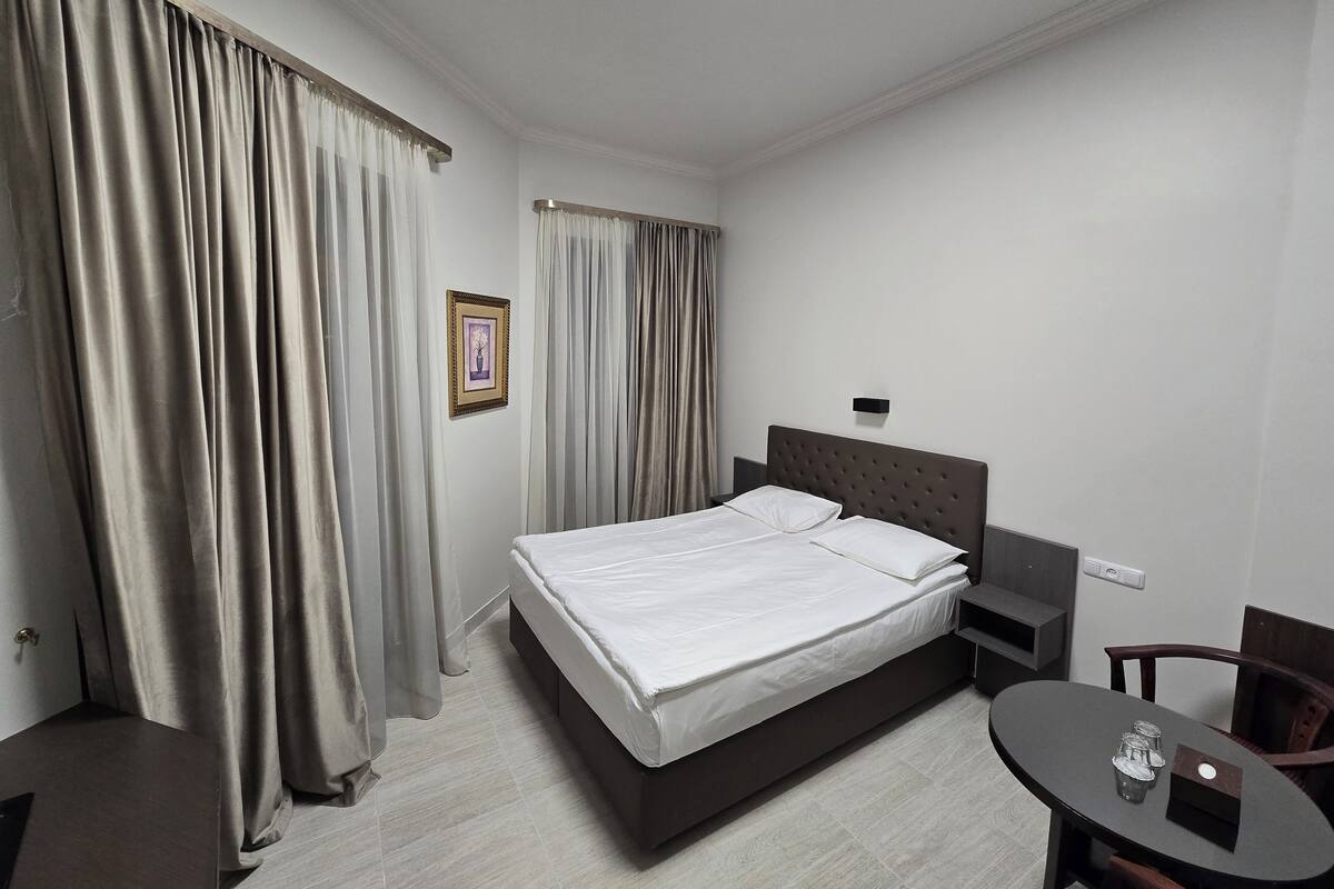 Une chambre d’hôtel avec un lit, une table de chevet, une chaise, une petite table et un tableau au mur.