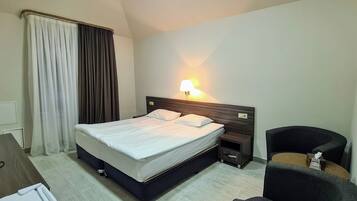 Ein Hotelzimmer mit Bett, Nachttisch, Lampe, Stuhl und Schreibtisch mit Computer.