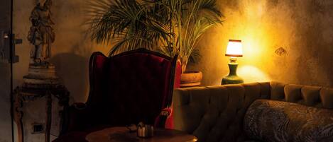A cozy room with a plush red chair, a small round table, a sofa, a lamp, and a large potted plant.
