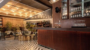 A bar area with a wooden counter, seating with cushioned chairs, a patterned floor, and shelves with wine bottles and glasses. - Casa Suzanna (Tel Aviv)