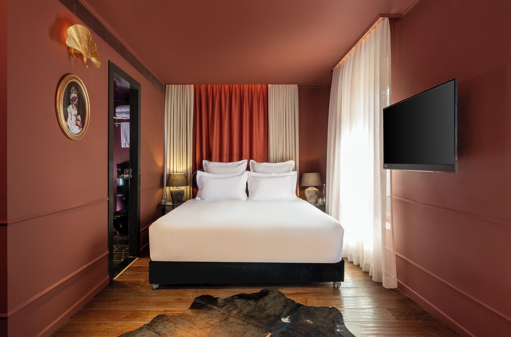 A modern hotel room with a large bed, a flat-screen TV, and a view of the city.
