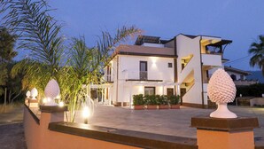 A modern two-story house with a balcony, potted plants, and a well-lit entrance. - Il Girasole Capo d'Orlando (Capo d'Orlando)