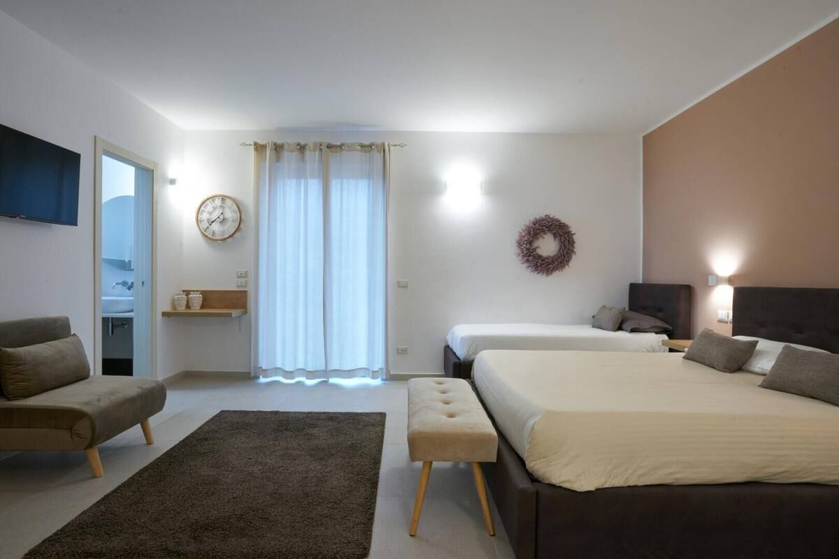 A modern bedroom with two beds, a sofa, a small table, and a TV.