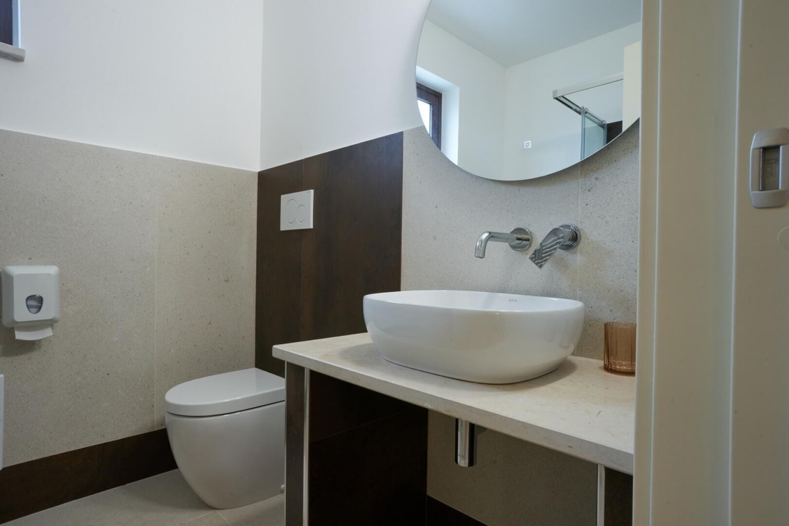 Ein modernes Badezimmer mit einem weißen Waschbecken, einer Toilette und einem Spiegel über dem Waschbecken.