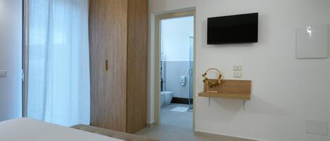 A hotel room with a bed, a wooden wardrobe, a TV mounted on the wall, and a small wooden shelf with a decorative item.