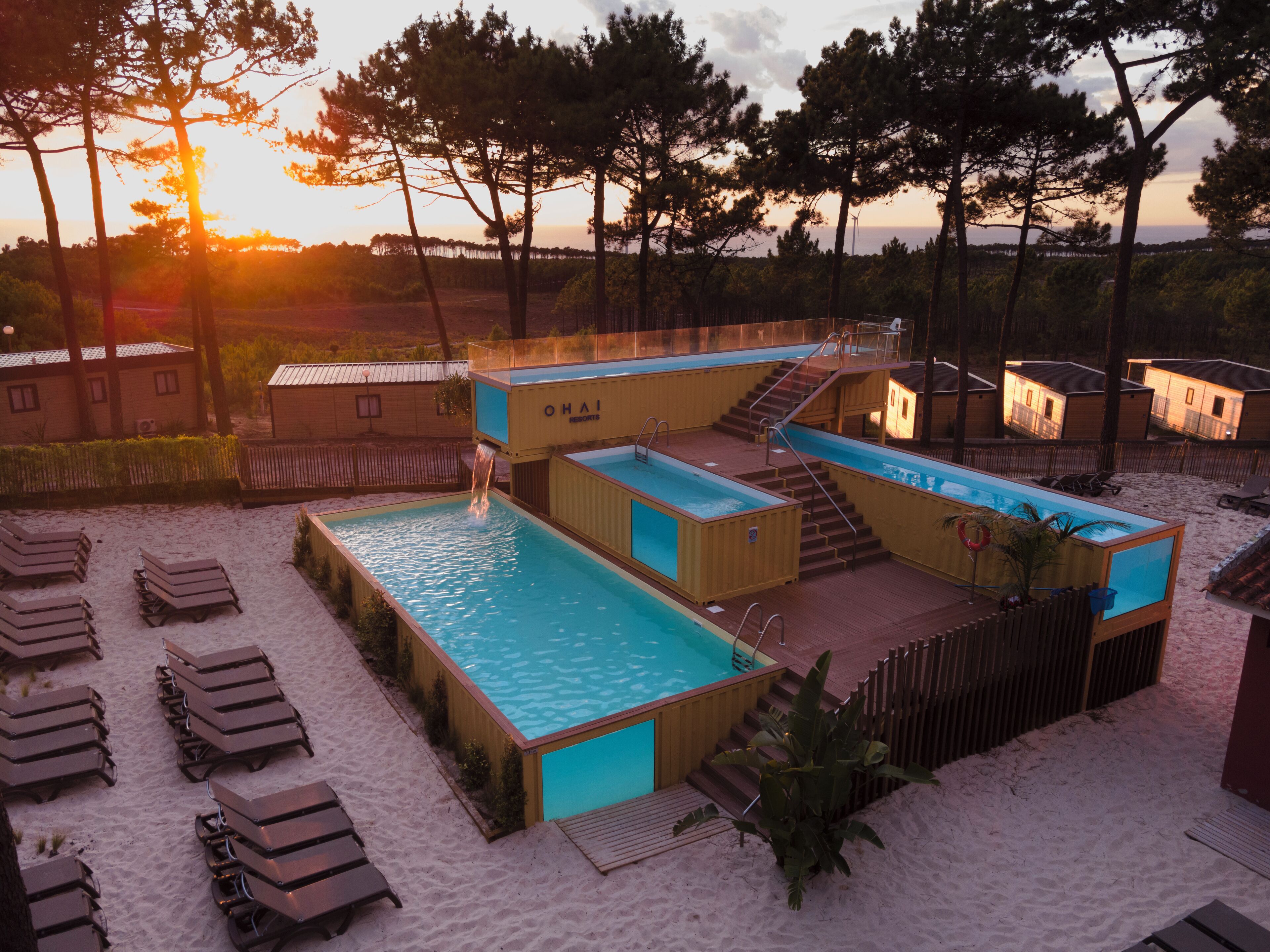A pool area with multiple swimming pools, lounge chairs, and wooden cabins.