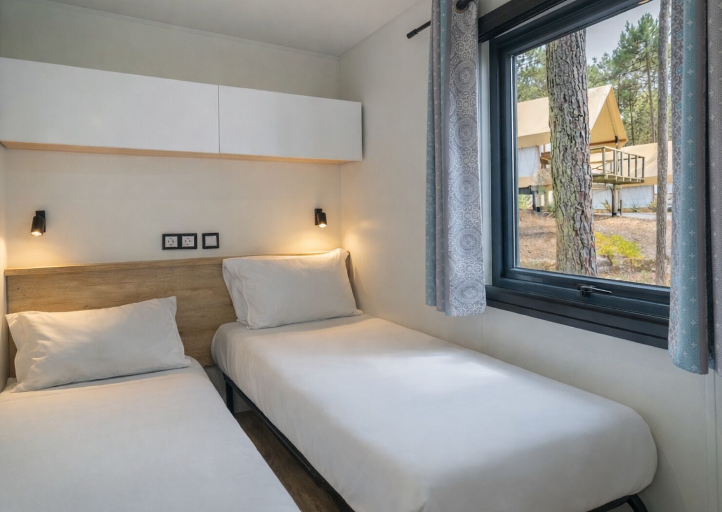Un dormitorio con dos camas, una ventana con cortinas y vistas a tiendas de campaña al aire libre.