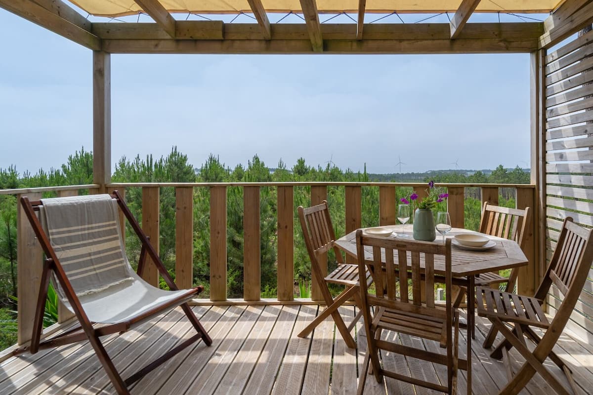 En träveranda med ett bord och stolar, en bekväm fåtölj och utsikt över landskapet.