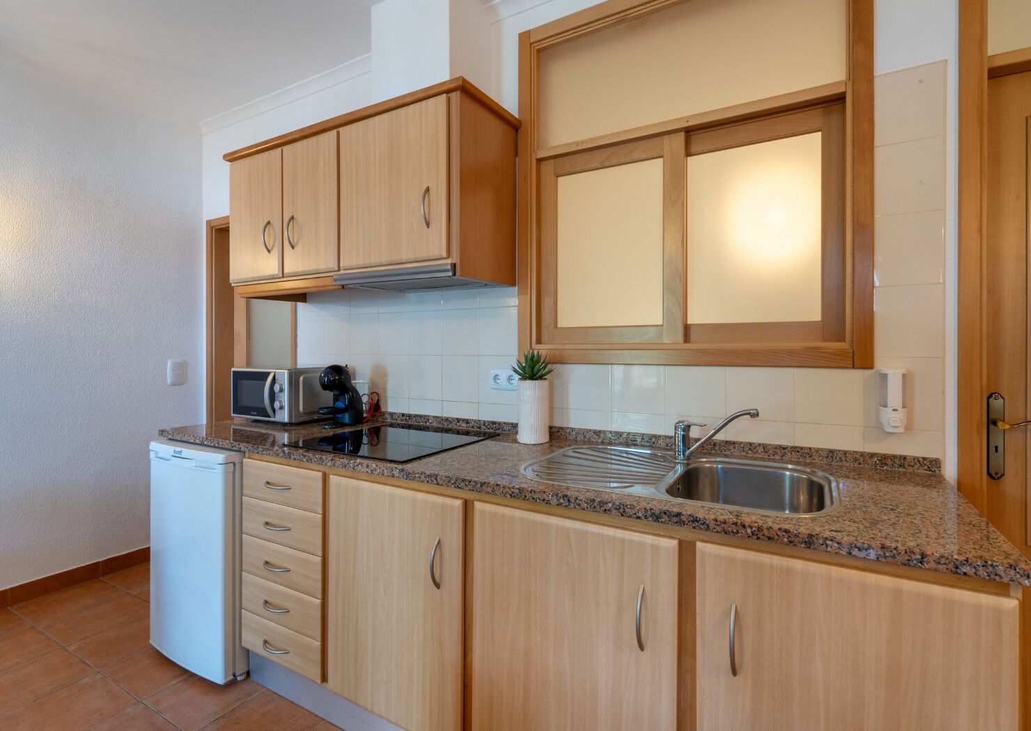 A compact kitchen with wooden cabinets, a built-in microwave, a sink, and a small refrigerator.