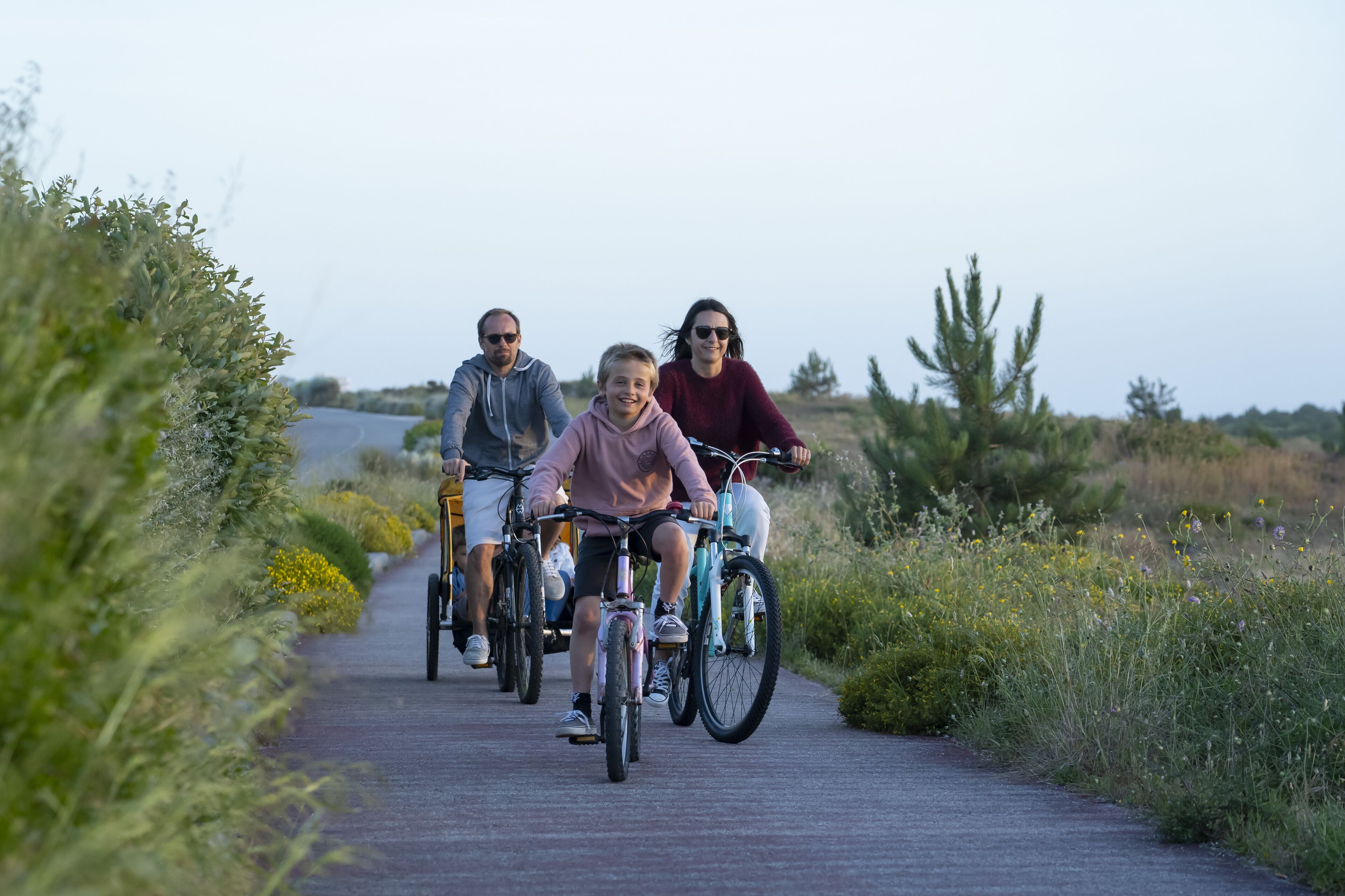 A group of people riding bicycles on a paved path surrounded by greenery.