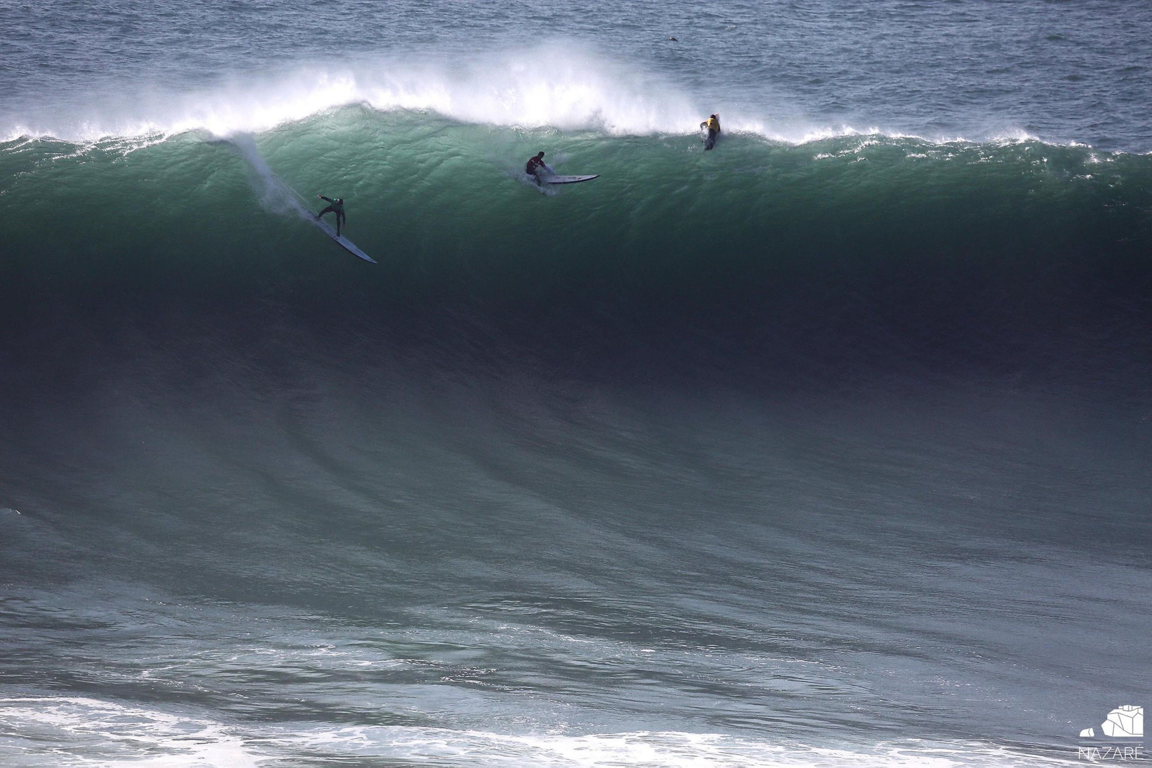 Uma onda grande com três surfistas.