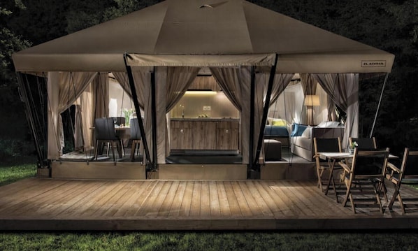 Alojamento em tenda com um alpendre de madeira, cozinha compacta e áreas de estar.