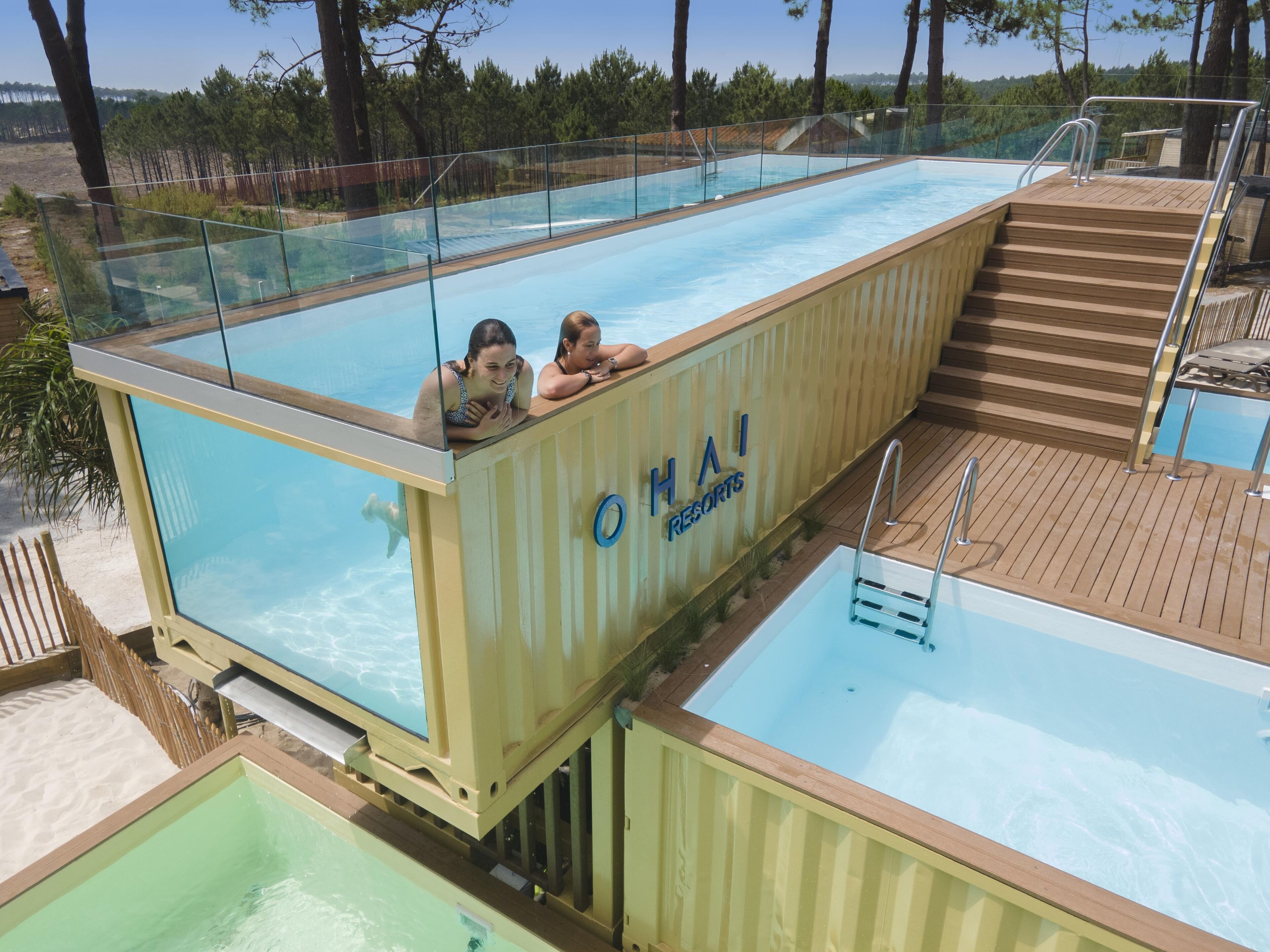 A glass-enclosed swimming pool at HAI Resorts with a wooden deck and a separate pool area.