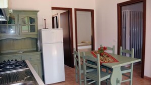 A compact kitchen with a gas stove, a white refrigerator, and a dining table with chairs. - Baia dei Canonici (Borgia)
