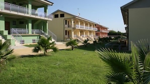 A hotel with a green facade, multiple balconies, and a central courtyard with palm trees. - Baia dei Canonici (Borgia)