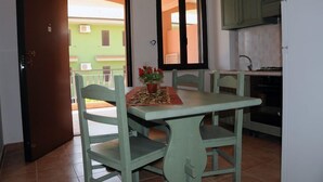 A dining area with a table and chairs, a window with curtains, and a view of a green building outside. - Baia dei Canonici (Borgia)