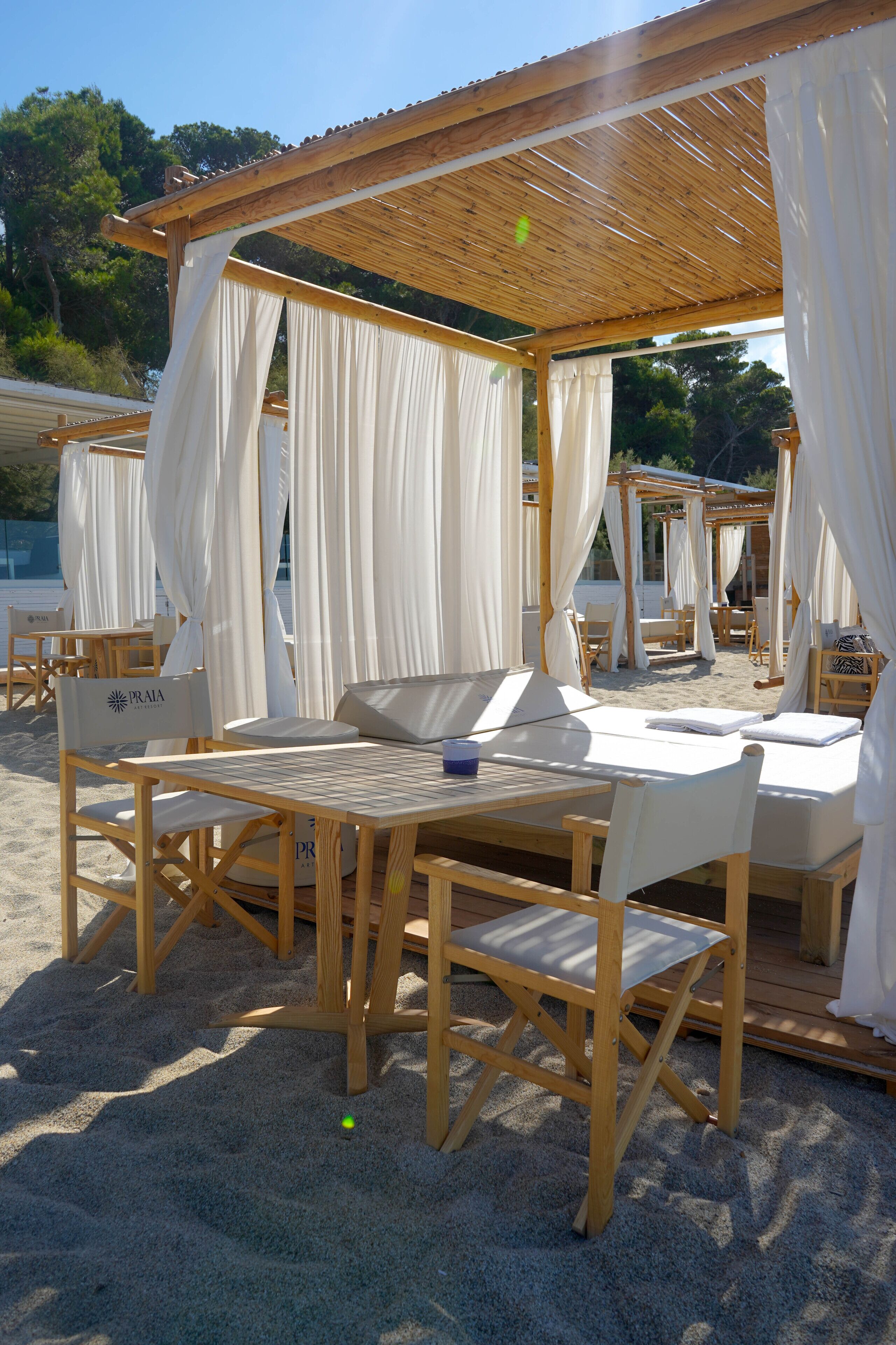 Una cabaña frente al mar con muebles de madera y cortinas blancas.