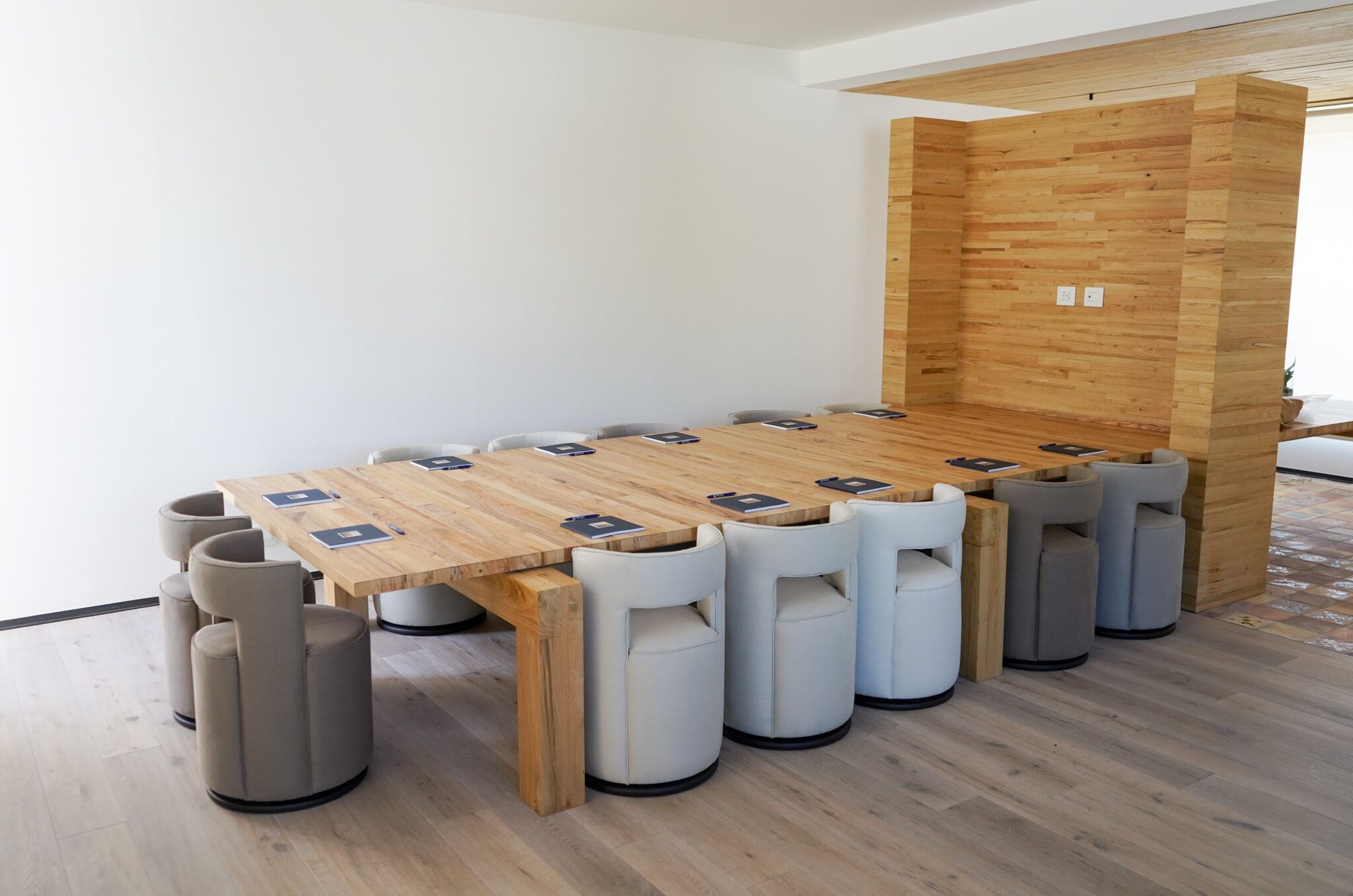 Una sala de reunions moderna amb una taula de fusta i sis cadires, cadascuna amb un bloc de notes i una ploma.