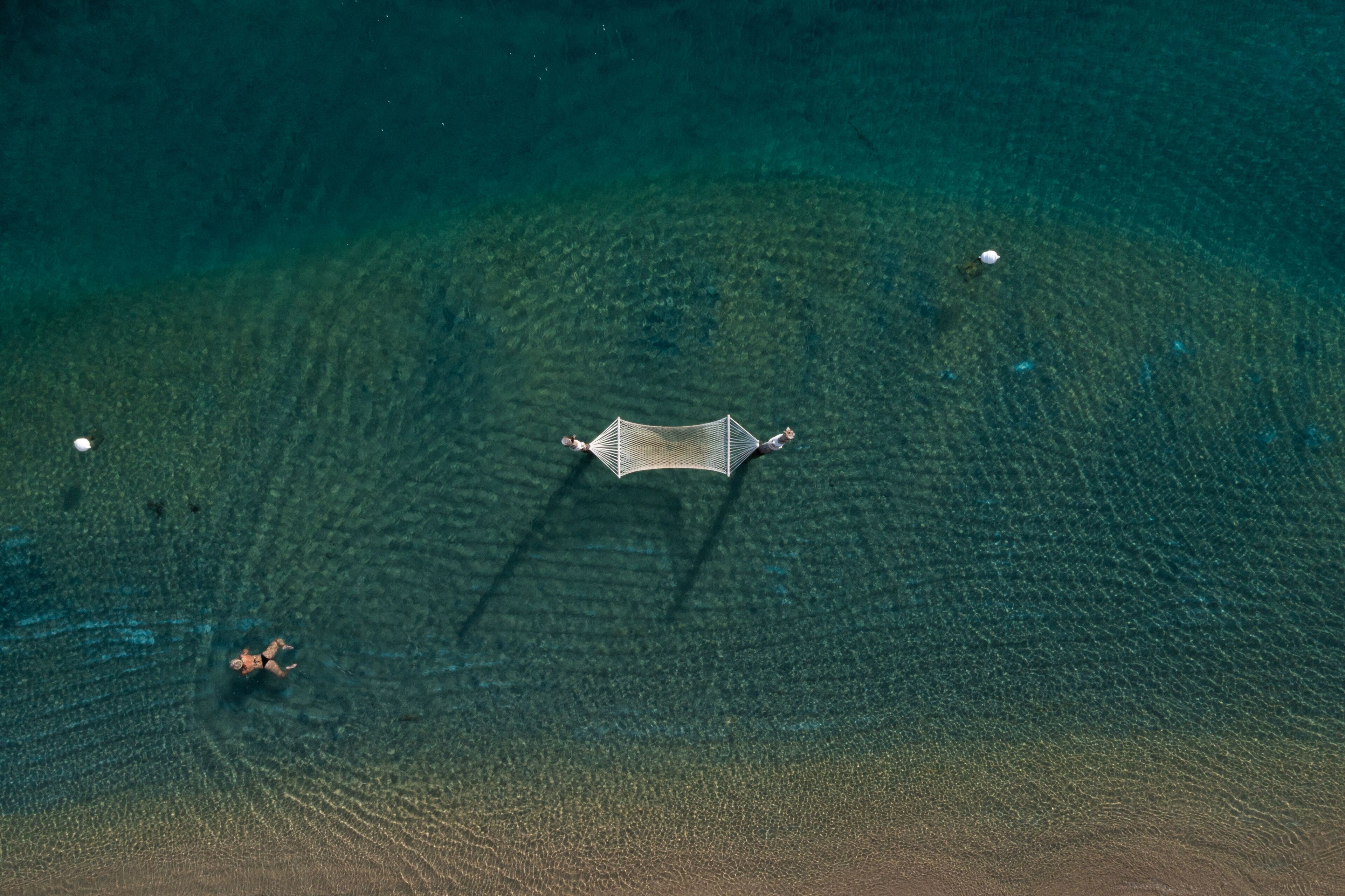 Vista aérea de una playa con una hamaca y una persona nadando.