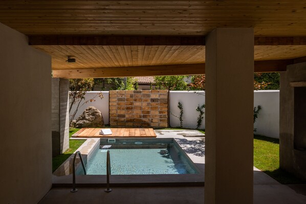 A modern outdoor pool area with a wooden deck, a stone wall, and a concrete pool.