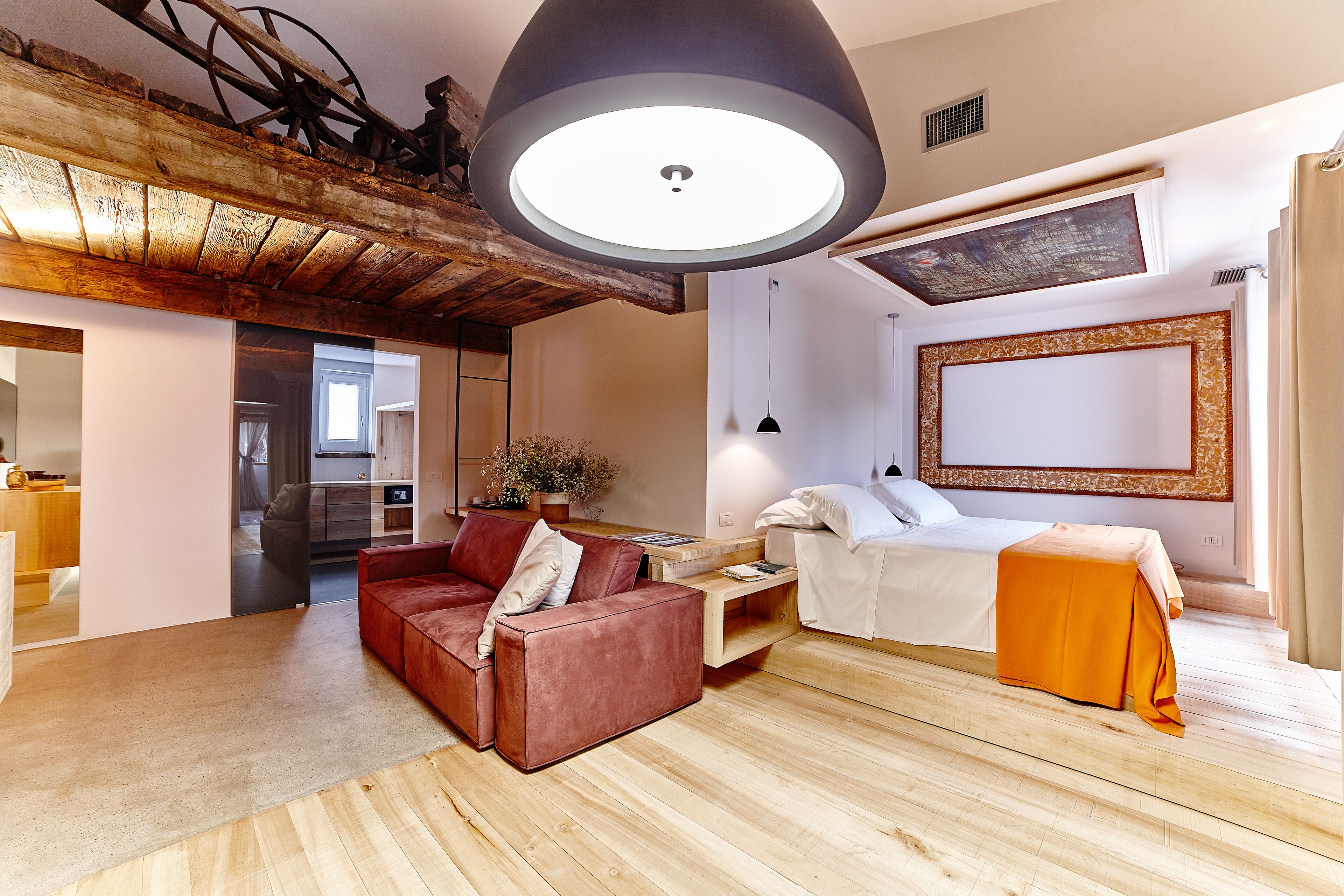 Una sala de estar moderna con techo de madera, un sofá rojo, una cama blanca y una obra de arte grande en la pared.