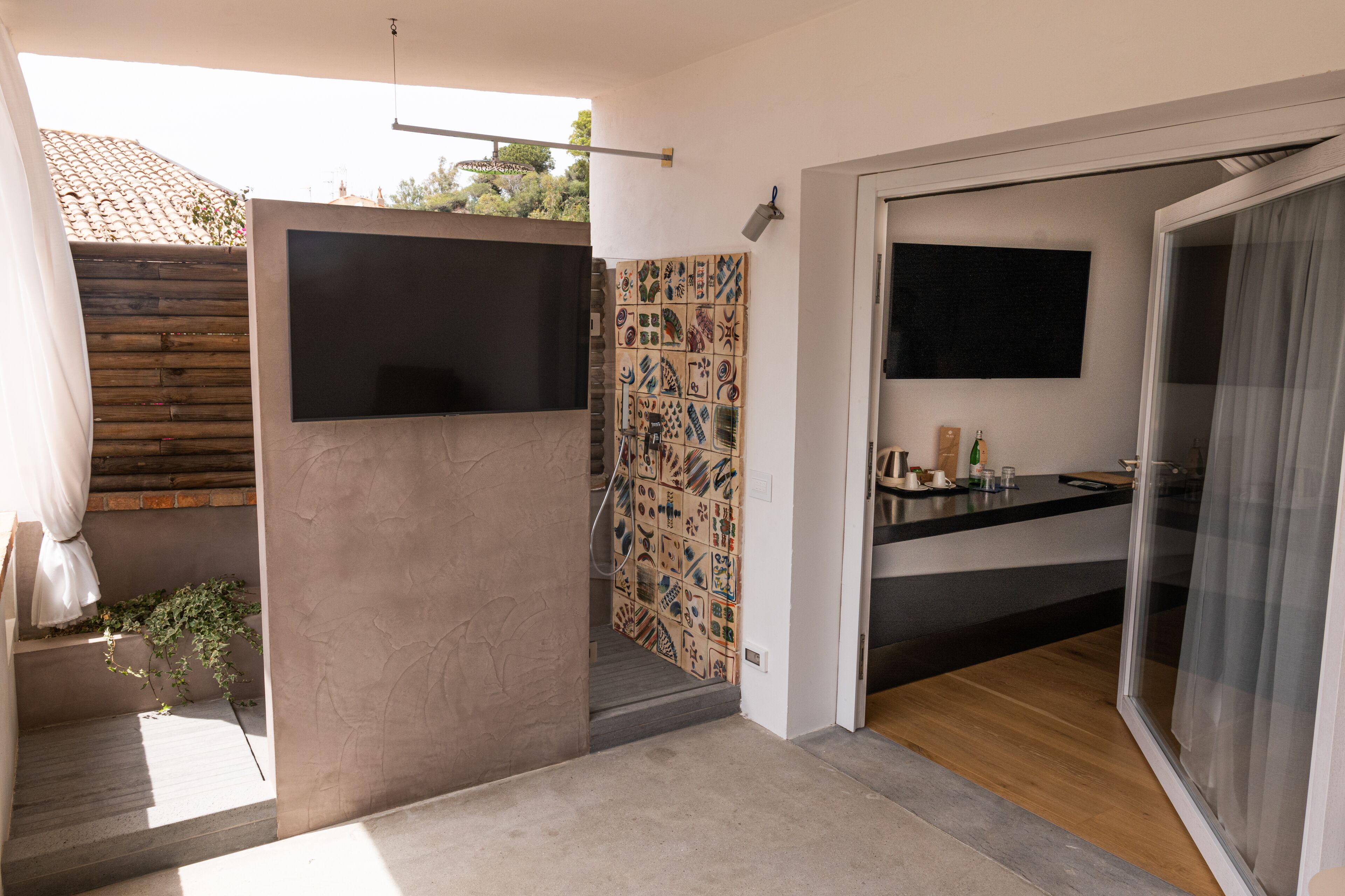 A modern bathroom with a shower, a sink, and a toilet. There is a wooden bench and a potted plant.
